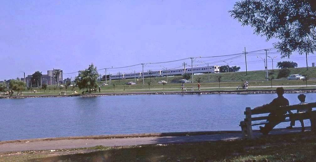 AAA PHOTO - TORONTO - GRENADIER POND HIGH PARK - COUPLE SITTING ON BENCH - GO COMMUTER TRAIN PASSING IN DISTANCE - 1969